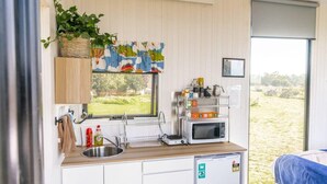 A compact kitchenette with a sink, microwave, and small refrigerator. - Tiny Balloon House by Tiny Away (Canowindra)