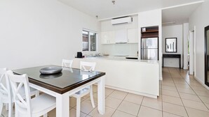 A modern kitchen with white cabinetry, a central island, and a dining area with a glass table and white chairs.