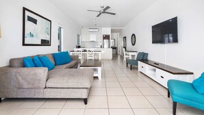 A modern living room with a grey sofa, a teal armchair, and a dining area in the background.