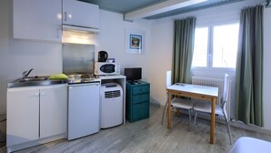 Una cocina compacta con armarios blancos, un microondas, un refrigerador pequeño y una mesita de noche color aguamarina.