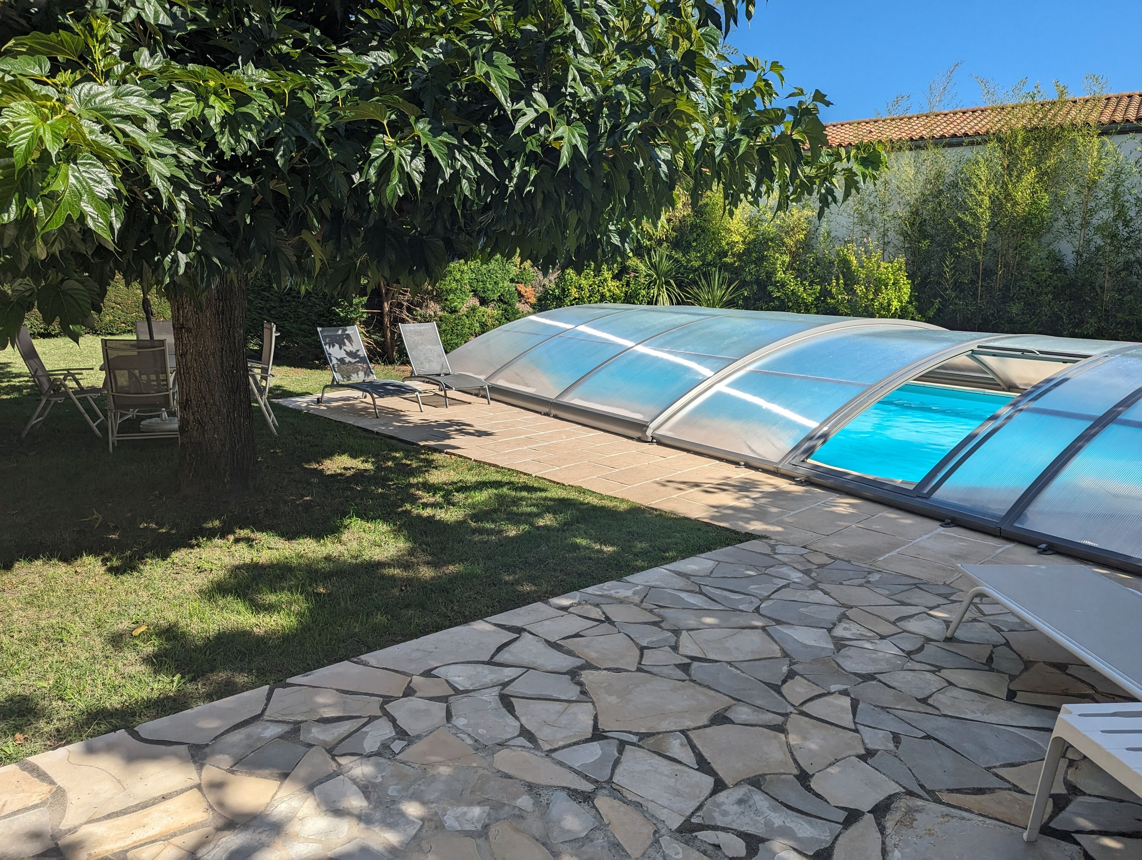 Une serre dotée d’une piscine, d’une terrasse en pierre et d’un espace salon extérieur.