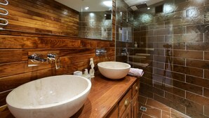 Un baño con paneles de madera, un lavabo grande de color blanco y una zona de ducha con mampara de vidrio.