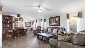 A spacious living room with a brown leather sofa, a wooden coffee table, and a dining area with chairs and a small table. - The Villa - Amazingly Comfortable King Beds (Alpine)