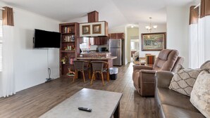 A modern living room with a sofa, a coffee table, and a TV. There is a kitchen area with a fridge, stove, and dining table. - The Villa - Amazingly Comfortable King Beds (Alpine)