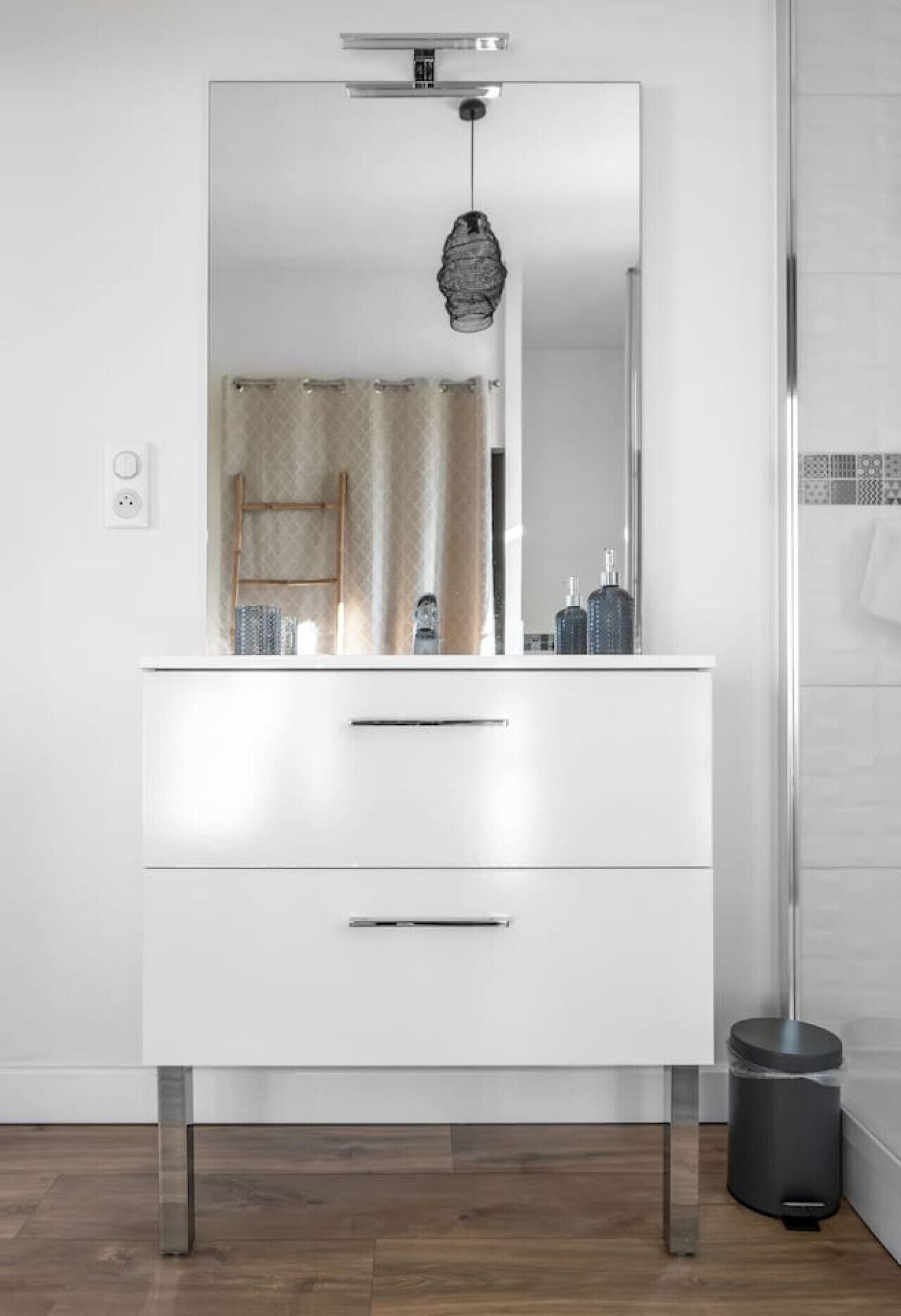 Un baño moderno con tocador blanco, espejo y lámpara colgante.