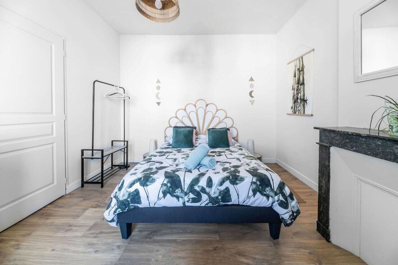 Un dormitorio con cama, mesita de noche, lámpara colgante y una obra de arte en la pared.