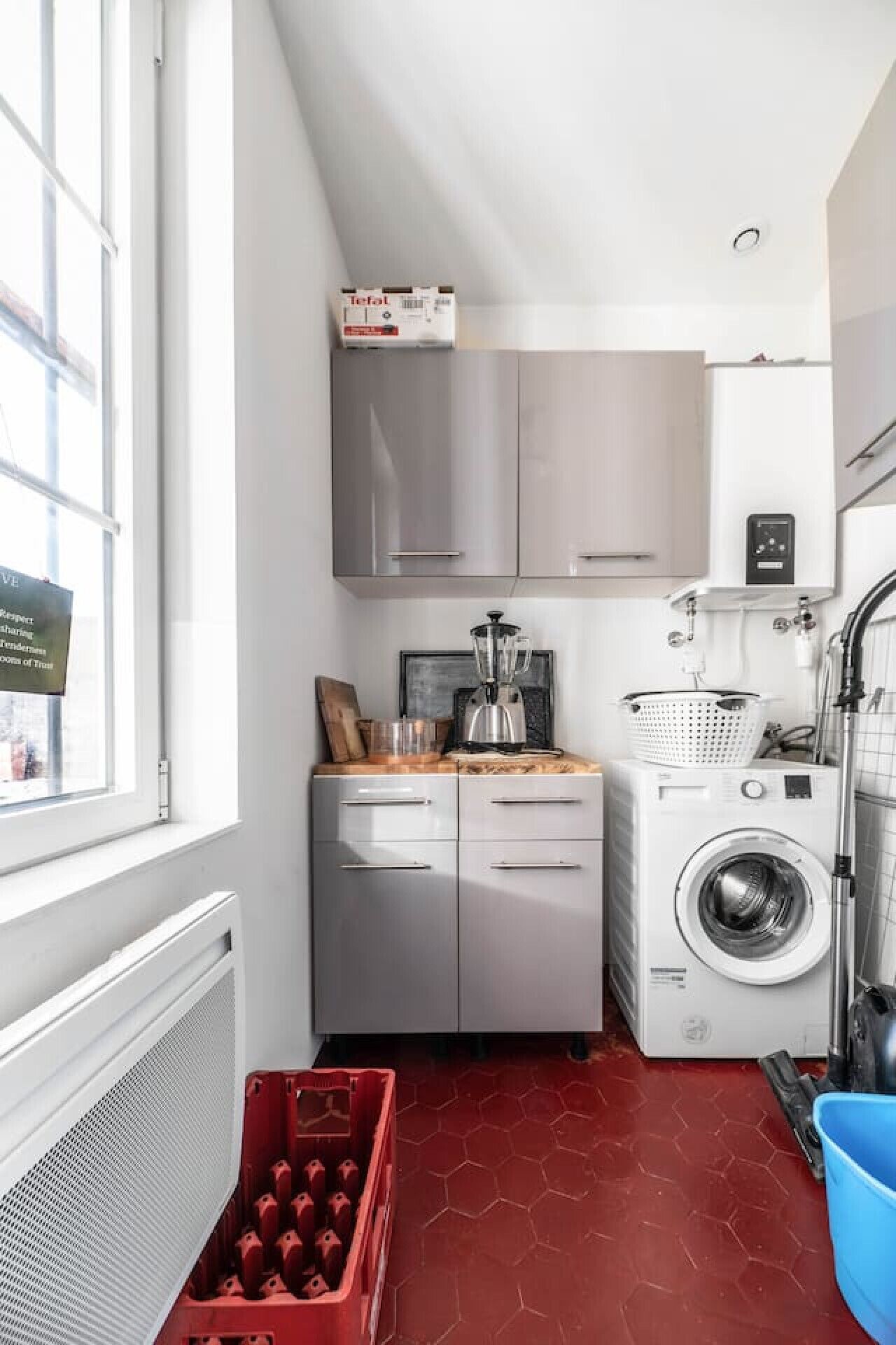 Een compacte keuken met roestvrijstalen apparatuur, een rode zeshoekige vloer en een raam met uitzicht.