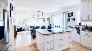 A modern kitchen with white cabinetry, a large island, and a dining area with blue chairs. - Tropical Paradise, walking distance to the beach and heated pool! (Hollywood)