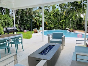 Um pátio externo com piscina, espreguiçadeiras, churrasqueira e lareira.