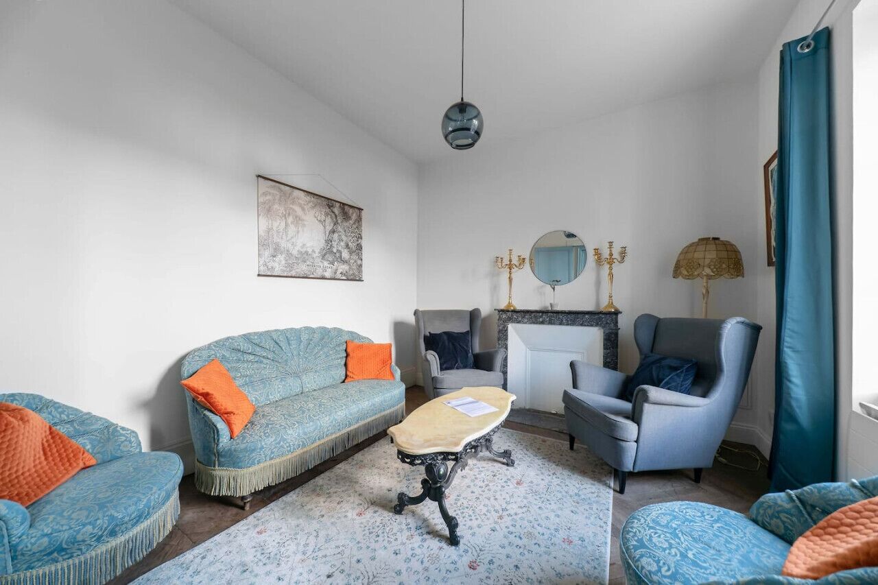 En stue med sofa, lænestol og et lille bord. Der er en pejs med et spejl over.