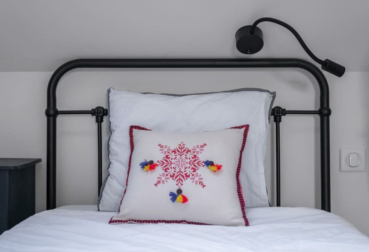 Un lit avec un oreiller blanc orné d’un motif en forme de flocon de neige rouge et de franges colorées.