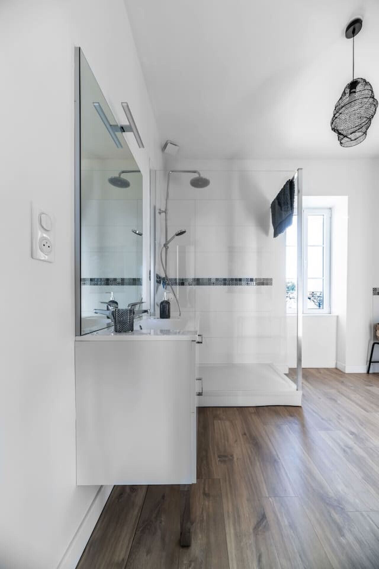Un baño moderno con un espejo grande, una ducha y un lavamanos.