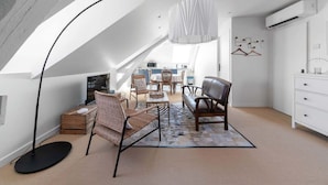 A modern loft bedroom with a sloped ceiling, a dining area with wicker chairs, a sofa, and a hanging light fixture. - Grande Maison Design, jardin, patio et parking (Gannat)