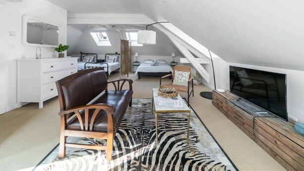 A spacious loft bedroom with a large bed, a seating area with a leather sofa, a TV, and a view of the city through skylights. - Grande Maison Design, jardin, patio et parking (Gannat)