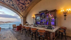 Zona de bar con vistas al mar, taburetes y una barra decorativa.