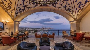 Un salón lujoso con sofás y sillones de cuero, piso con diseño y vista al mar y al paisaje urbano a través de un arco ornamentado.