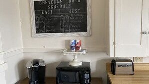 Un piano di lavoro in cucina con una macchina da caffè, un forno a microonde e un tostapane. Una lavagna con un orario dei treni è fissata al muro sopra il piano di lavoro.