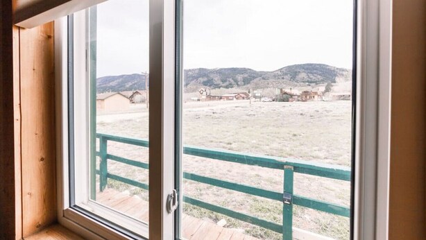 A window with a view of a fenced area and distant buildings. - Queen Suite in Historic Centennial Hotel (Centennial)