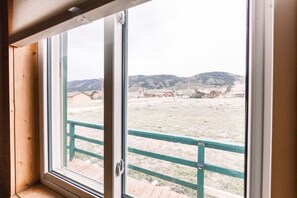 A window with a view of a fenced area and distant buildings. - Queen Suite in Historic Centennial Hotel (Centennial)