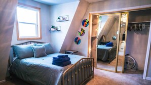 Een slaapkamer met een bed, een raam, een kast en een spiegel.