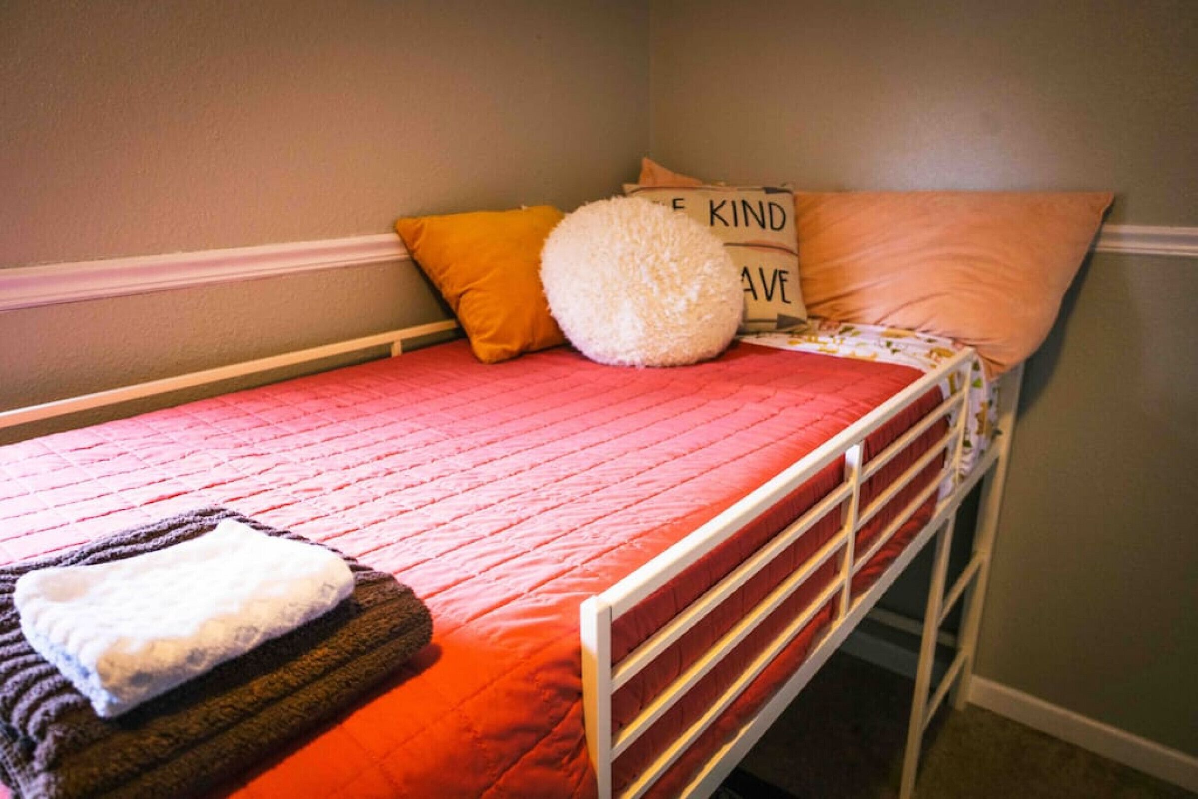 A single bed with a red quilt, a white pillow, and a fluffy white pillow.
