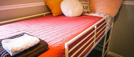 A single bed with a red quilt, a white pillow, and a fluffy white pillow.