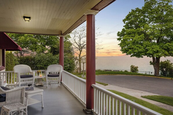 A covered porch with wicker furniture and a view of the sunset over the water.