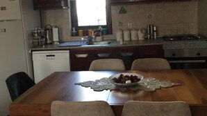 A kitchen with dark wooden cabinets, a stainless steel refrigerator, a dishwasher, a gas stove, and a dining table with four chairs. - Beachside House in Gundogan (Bodrum)