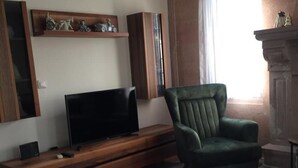 A living room with a television on a wooden stand, a green armchair, and a sofa. - Beachside House in Gundogan (Bodrum)