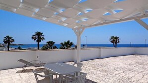 A covered patio with a view of the sea, featuring a table and chairs, and palm trees in the background. - VILLA SUNSET - Villa facing the sea (Torre Suda)