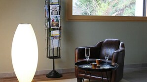 A room with a dark leather armchair, a small round table with two glasses, a standing book rack with travel guides, and a large floor lamp. - Au NEUF MILLE, luxury studio **** 2 steps from the port of Perros-Guirec (Perros-Guirec)
