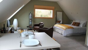 A room with a dining table set for two, a bed with a yellow blanket, a brown leather chair, and a window with a view of trees. - Au NEUF MILLE, luxury studio **** 2 steps from the port of Perros-Guirec (Perros-Guirec)