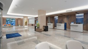 A modern hotel lobby with a reception desk, seating area, and a large window offering a view of the city. - Holiday Inn Express Qingdao Shibei by IHG (Qingdao)