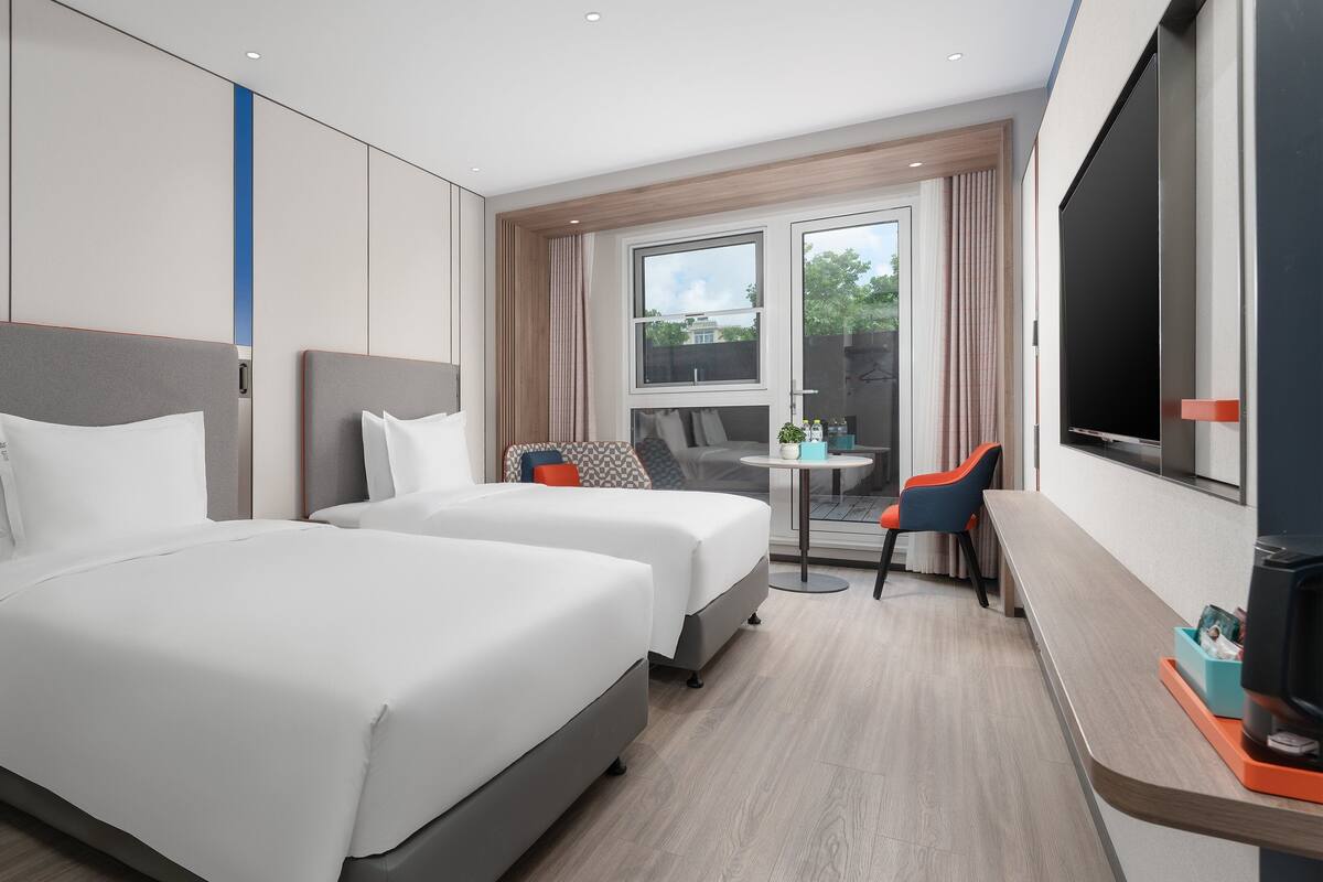 A hotel room with two beds, a desk, a chair, a TV, and a window with curtains.
