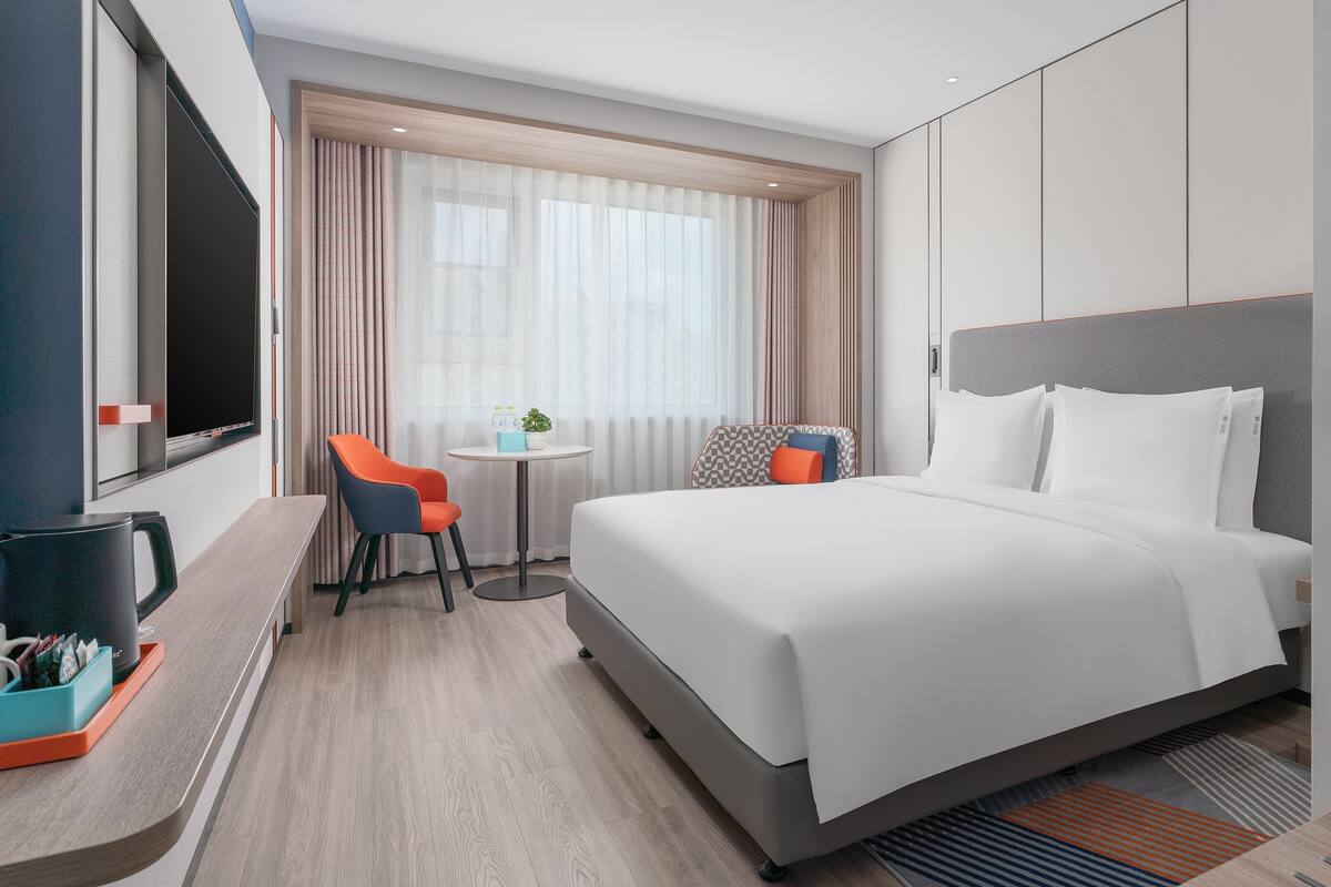 A hotel room with a bed, a desk, a chair, and a television.