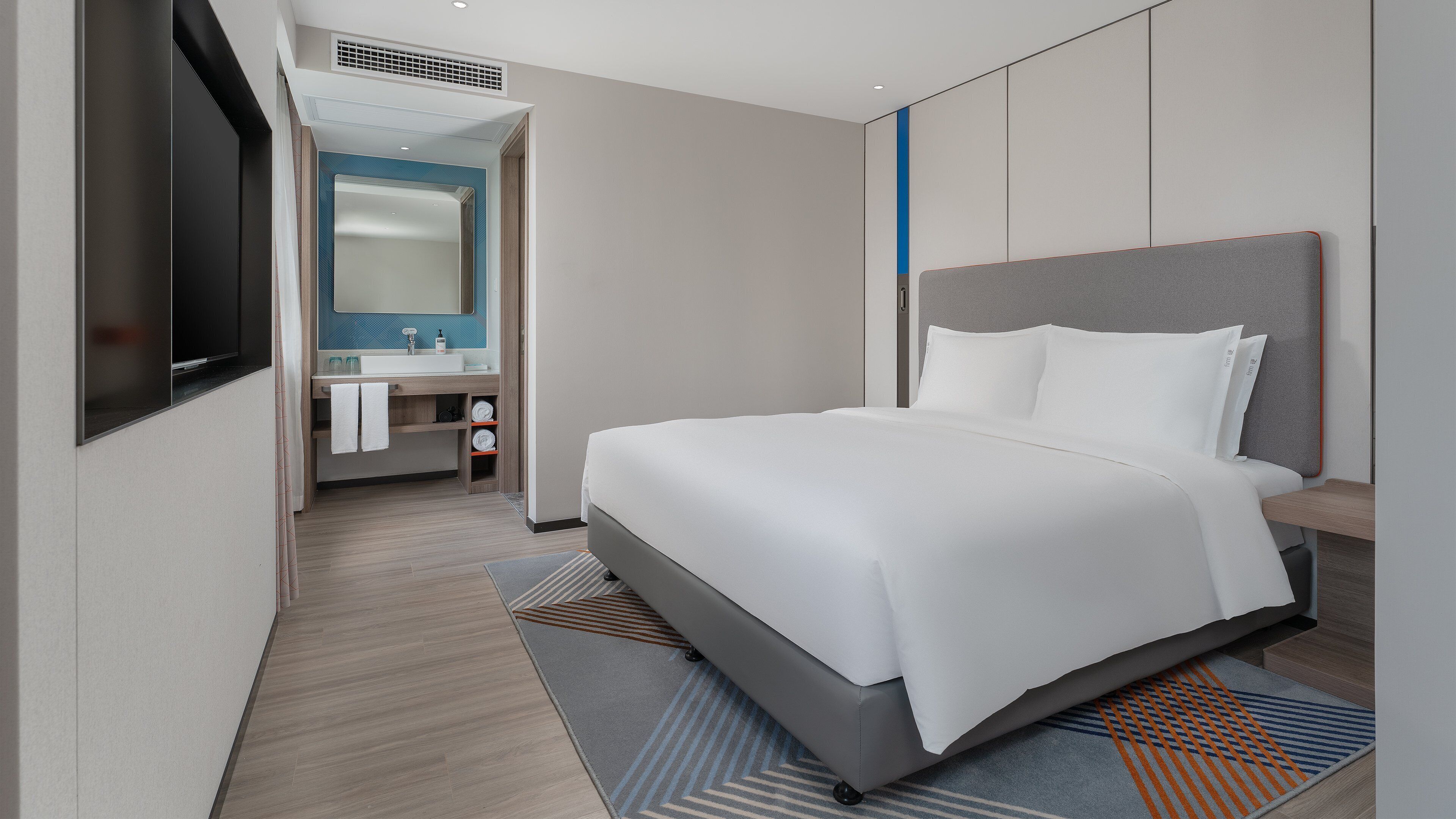 Una habitación de hotel moderna con una cama, un baño con espejo y un televisor.