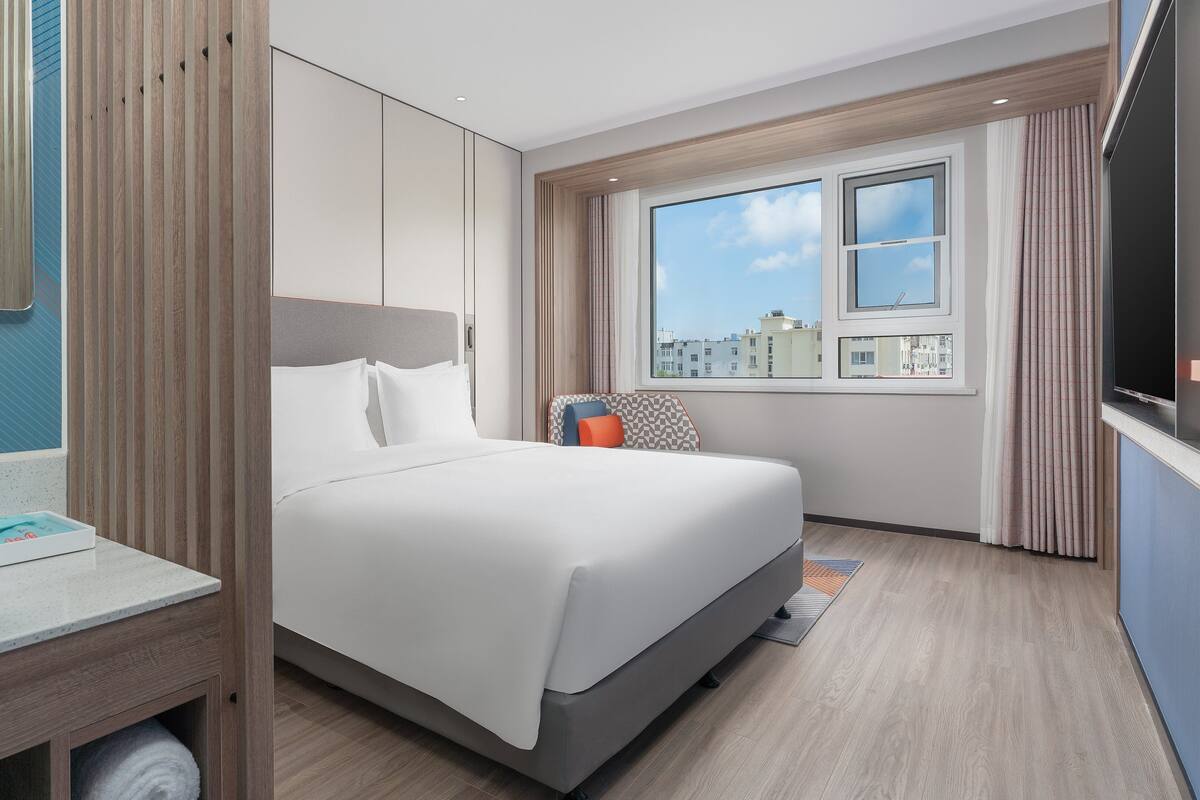 A hotel room with a bed, a bathroom with a sink, and a window with a city view.