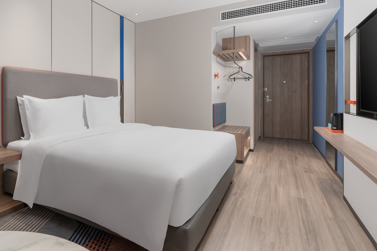 A modern hotel room with a large bed, bedside tables, a TV, and a wardrobe.