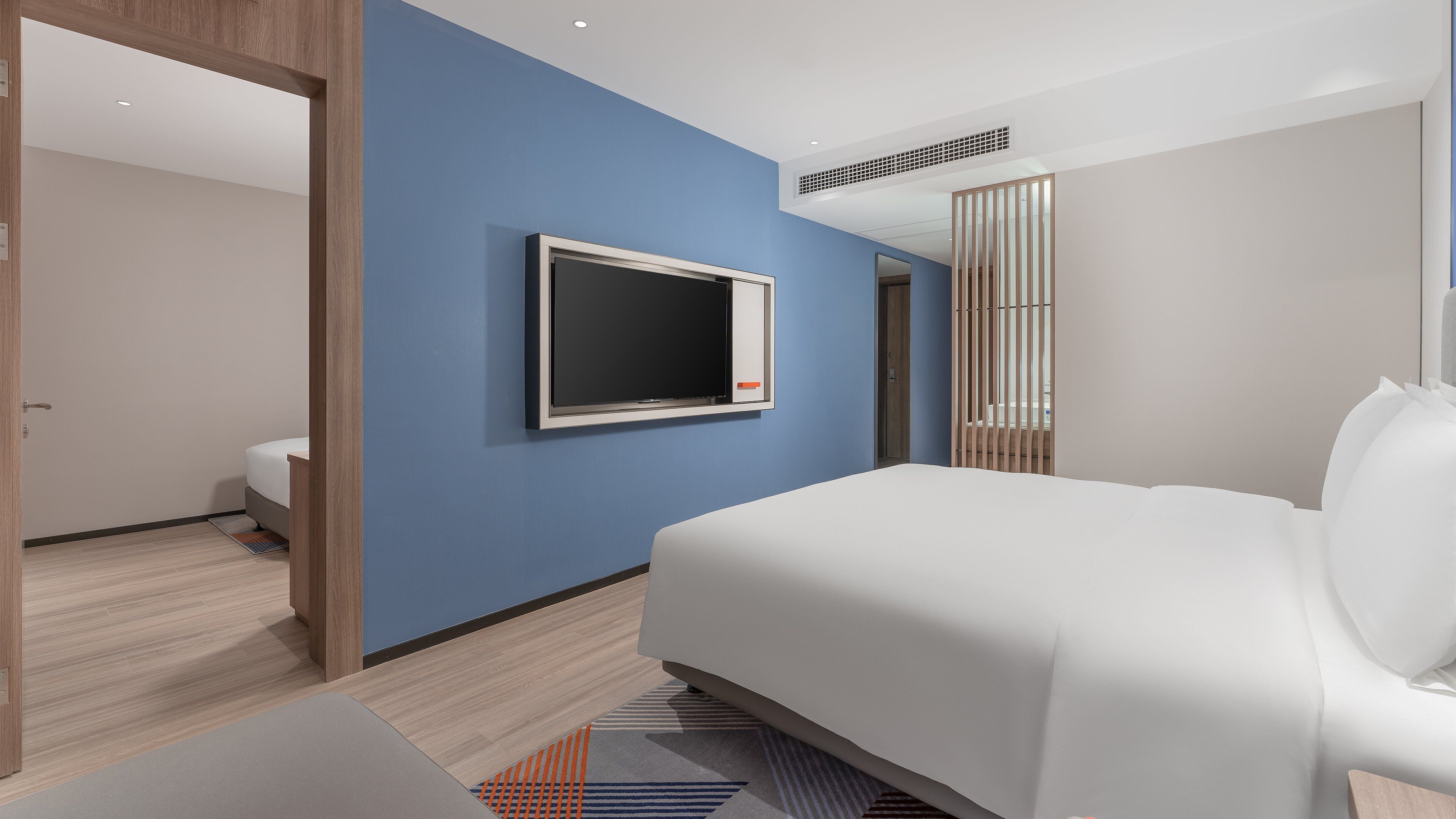 Una habitación de hotel moderna con una cama grande, un televisor de pantalla plana en la pared y una puerta de madera que da a otra habitación.