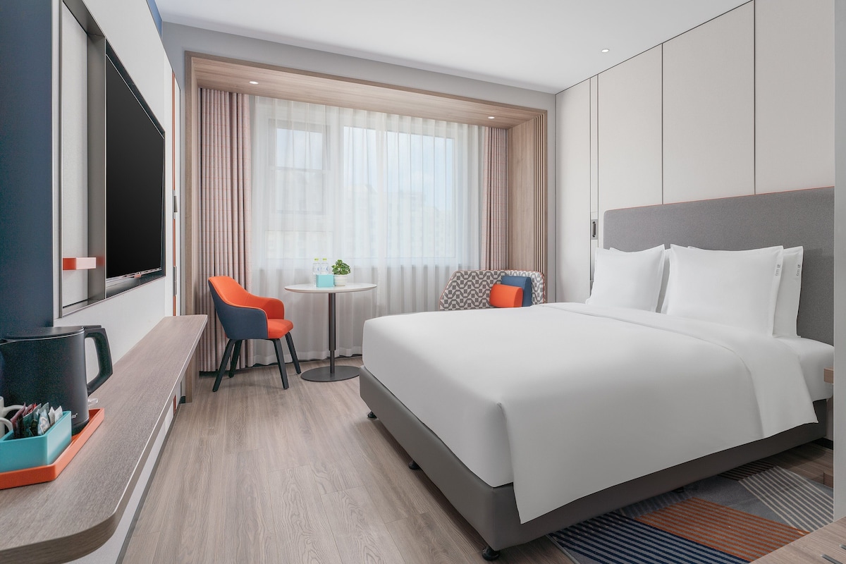 A hotel room with a bed, a desk, a chair, and a television.