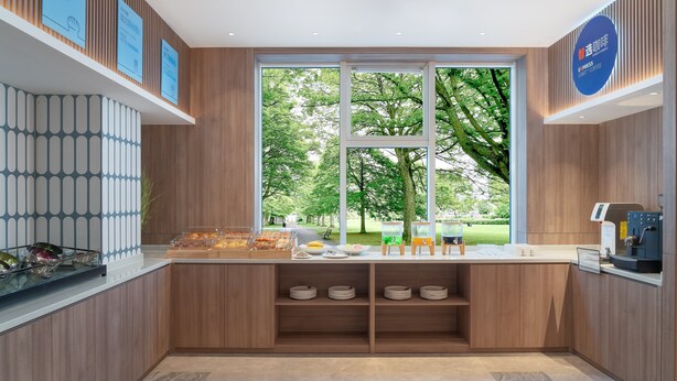 Un caffè moderno dall'arredamento in legno, con una grande vetrata che si affaccia su un parco e una macchina da caffè sul bancone.