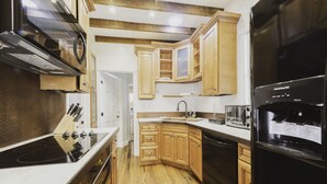 A modern kitchen with wooden cabinets, a black refrigerator, a stove, and a microwave. - Cozy Carriage House w/ Courtyard View ★ Victorian District ★ Near Forsyth Park
 (Savannah)