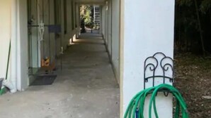 A corridor with a covered walkway, a metal gate, and a green garden hose coiled on a white column. - Cozy Carriage House w/ Courtyard View ★ Victorian District ★ Near Forsyth Park
 (Savannah)
