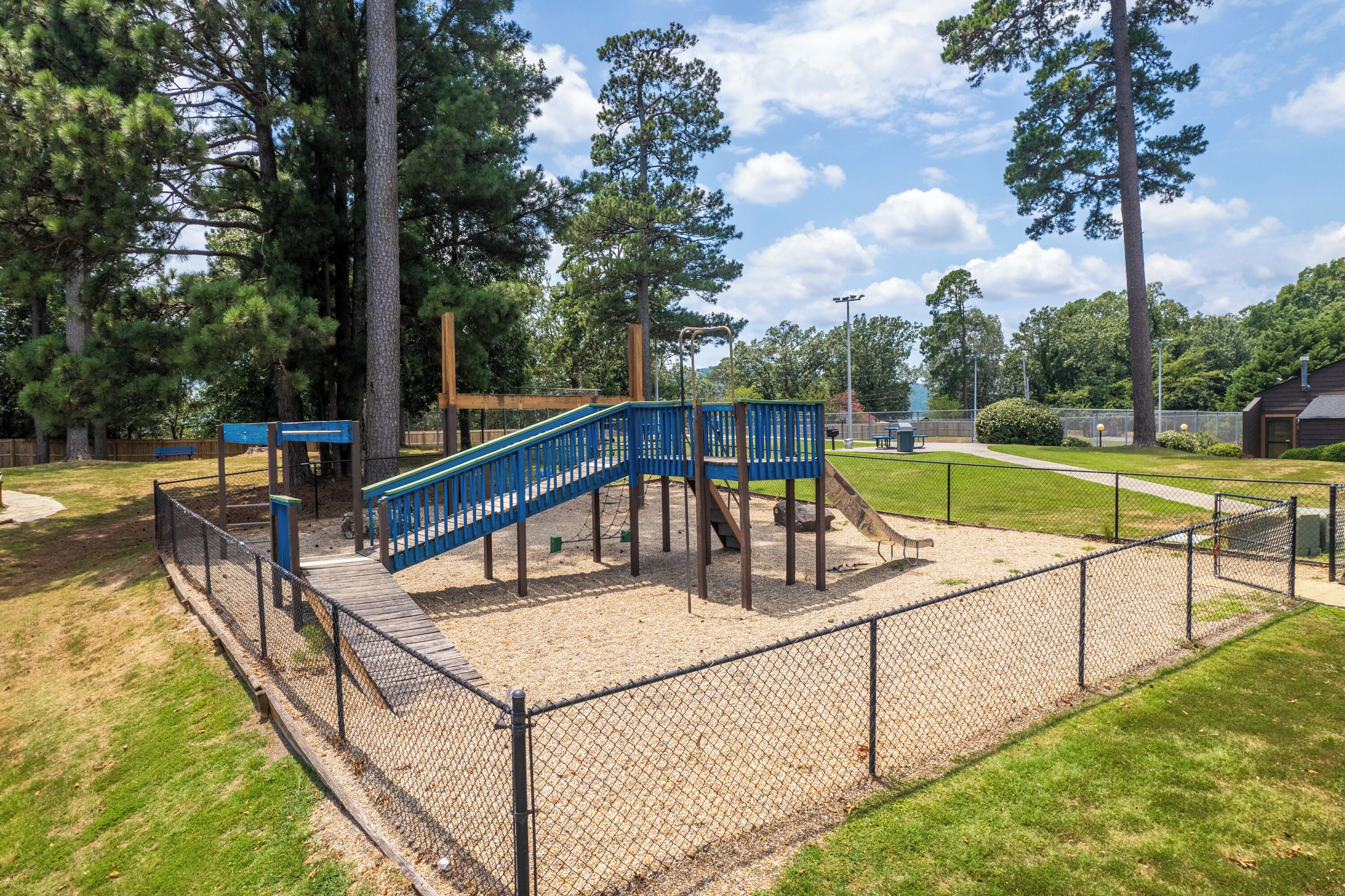 A playground with a blue staircase, surrounded by a chain-link fence and wooden structures.