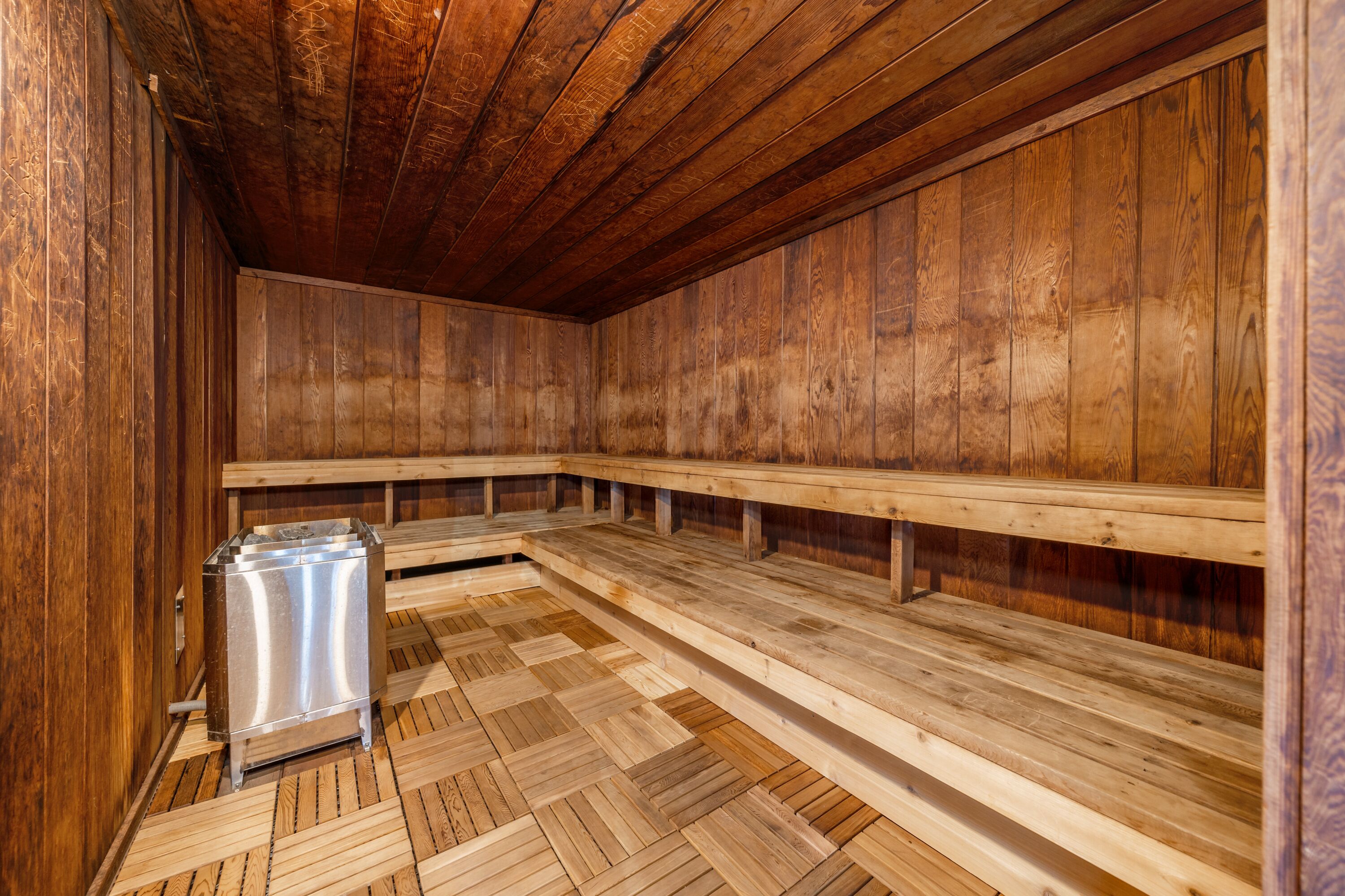 Una sauna con bancos de madera y un recipiente metálico, probablemente para agua o toallas.