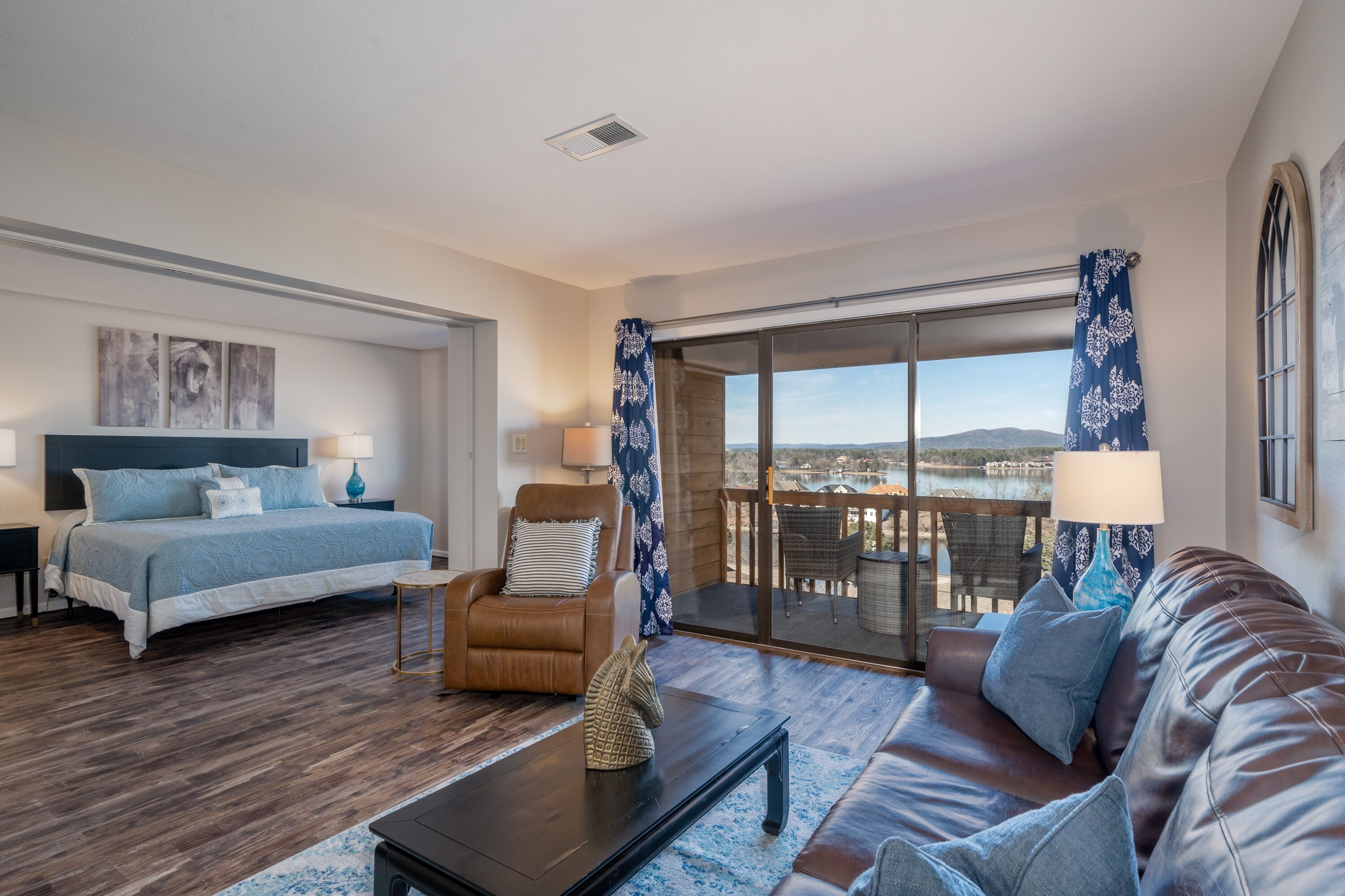 Een slaapkamer met een bed, een stoel, een bank en een balkon met uitzicht.