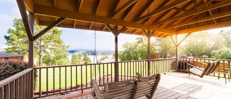 A wooden deck with a swing and two lounge chairs, overlooking a grassy area and a body of water.