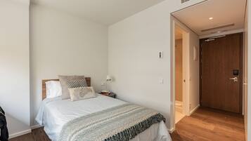 Un dormitorio con cama, mesita de noche, lámpara y una puerta que da a otra habitación.