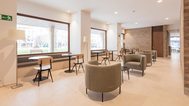 A modern hotel lobby with seating areas, large windows, and a brick accent wall. - Micampus Pamplona  (Pamplona)