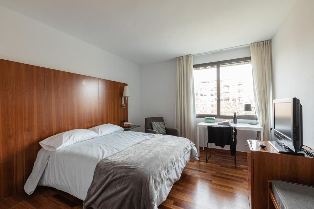 A hotel room with a large bed, a desk with a chair, a television, and a window with curtains.